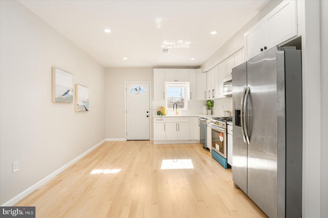 kitchen featuring appliances with stainless steel finishes, sink, light hardwood / wood-style flooring, and white cabinets