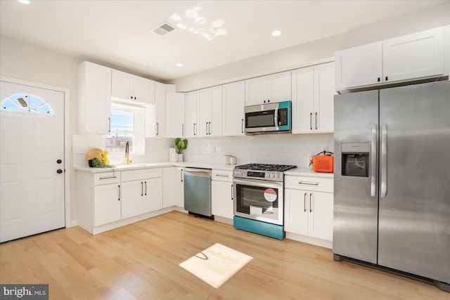 kitchen with tasteful backsplash, sink, white cabinets, stainless steel appliances, and light hardwood / wood-style flooring