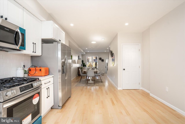 kitchen with appliances with stainless steel finishes, white cabinets, light wood-type flooring, and decorative backsplash