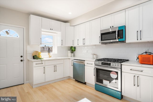 kitchen with sink, light stone counters, appliances with stainless steel finishes, light hardwood / wood-style floors, and white cabinets