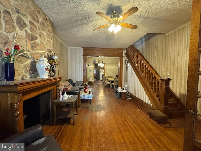 living room with hardwood / wood-style flooring, ceiling fan, a large fireplace, and a textured ceiling