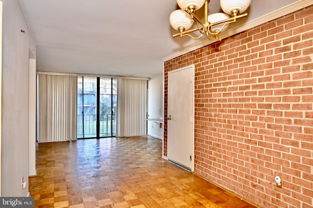 spare room with brick wall, a notable chandelier, a wall of windows, and parquet flooring