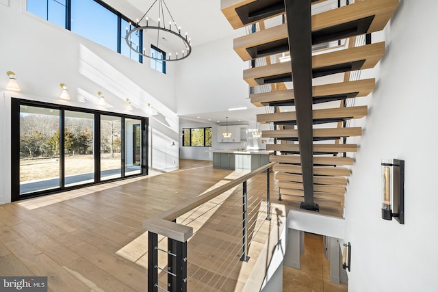 staircase with an inviting chandelier, hardwood / wood-style floors, and a towering ceiling