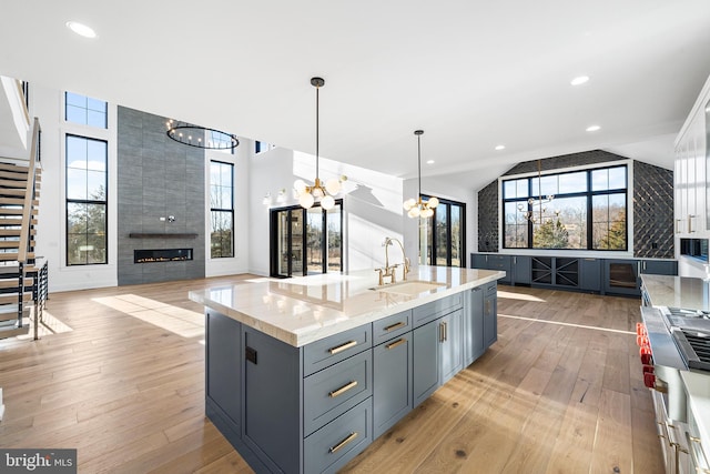 kitchen with pendant lighting, sink, a chandelier, light stone countertops, and a center island with sink