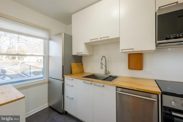 kitchen with butcher block countertops, white cabinetry, sink, decorative backsplash, and stainless steel appliances