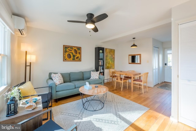 living room with an AC wall unit, ceiling fan, and light hardwood / wood-style flooring