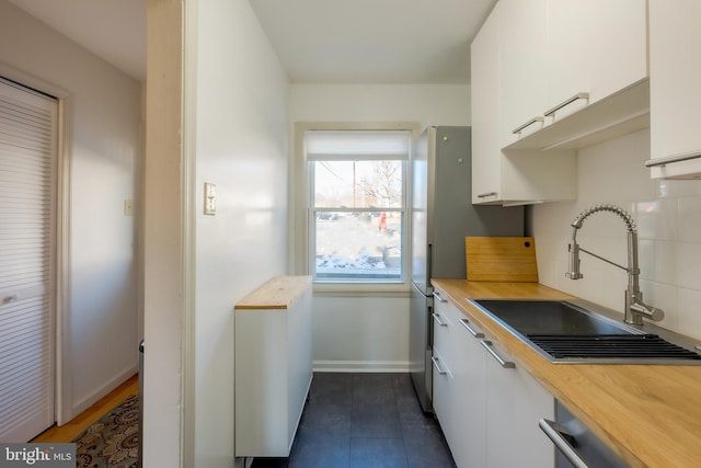 kitchen featuring butcher block counters, sink, dishwasher, white cabinets, and backsplash