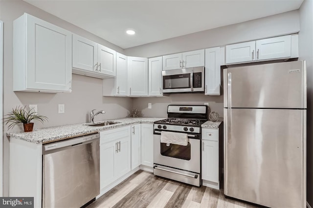 kitchen with sink, light stone counters, light wood-type flooring, stainless steel appliances, and white cabinets