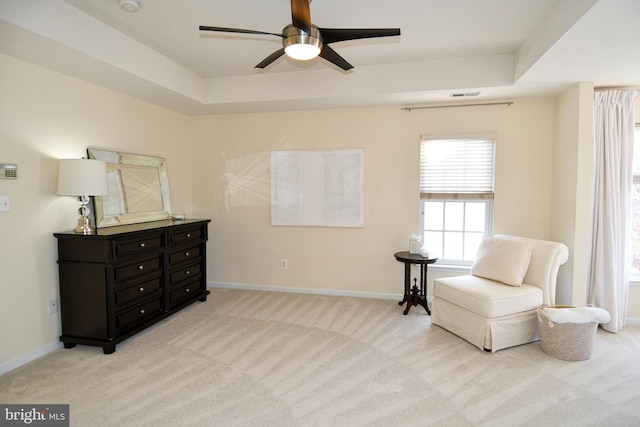 sitting room with ceiling fan, a tray ceiling, and light carpet