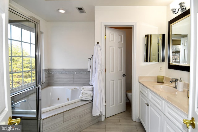 bathroom featuring vanity, tiled bath, and toilet