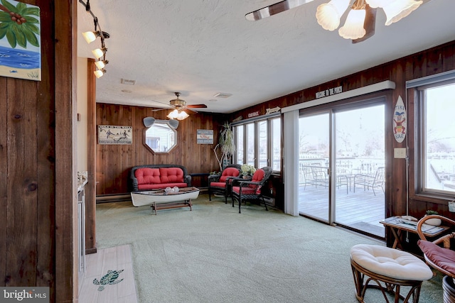 sitting room with plenty of natural light, wooden walls, ceiling fan, and carpet flooring