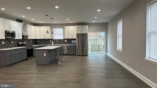 kitchen featuring stainless steel appliances, dark hardwood / wood-style floors, a center island, a kitchen bar, and decorative light fixtures