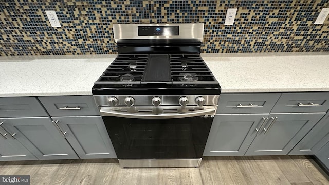 interior details with wood-type flooring, gray cabinetry, backsplash, and stainless steel gas stove