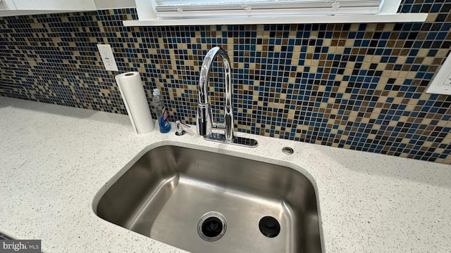 room details with light stone counters, sink, and backsplash