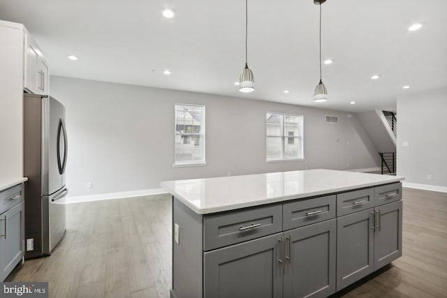 kitchen with gray cabinetry, decorative light fixtures, and stainless steel refrigerator