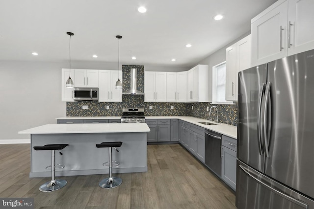 kitchen with gray cabinets, white cabinetry, hanging light fixtures, stainless steel appliances, and wall chimney exhaust hood