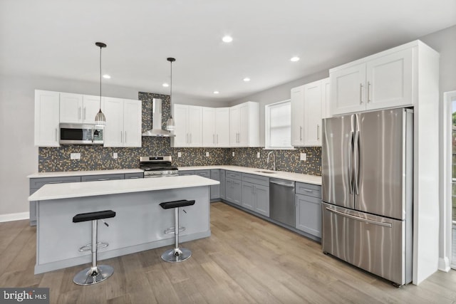 kitchen with pendant lighting, gray cabinetry, white cabinets, stainless steel appliances, and wall chimney range hood