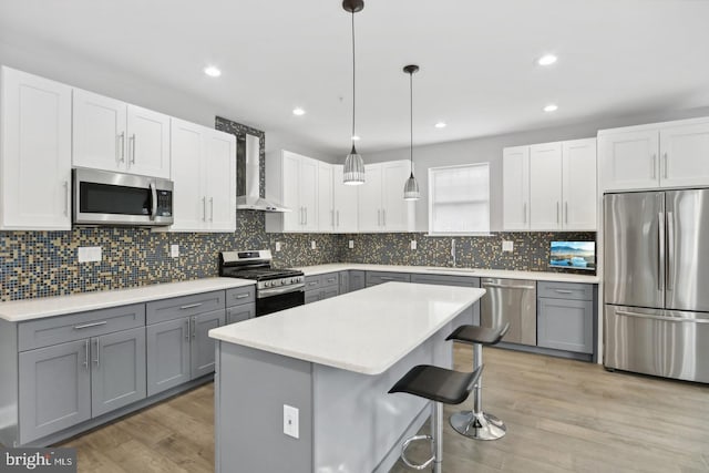 kitchen featuring appliances with stainless steel finishes, gray cabinetry, light hardwood / wood-style floors, a kitchen island, and decorative light fixtures