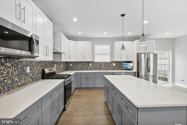 kitchen featuring gray cabinets, decorative light fixtures, white cabinets, stainless steel appliances, and light wood-type flooring