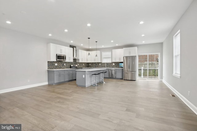 kitchen with gray cabinetry, hanging light fixtures, a kitchen bar, stainless steel appliances, and a kitchen island