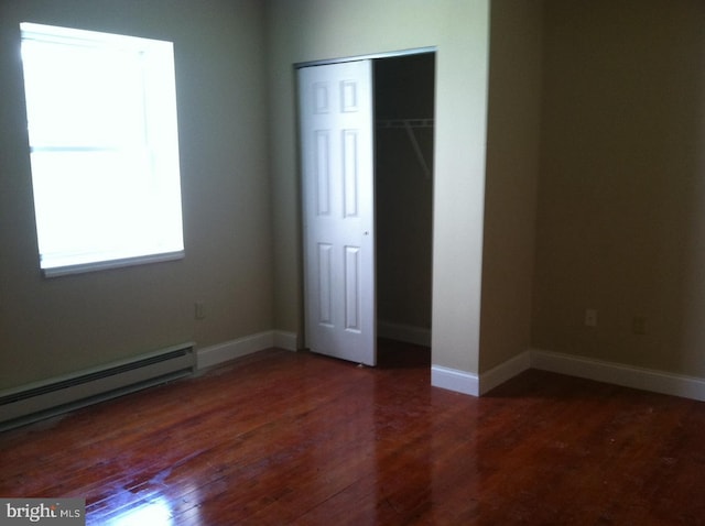 unfurnished bedroom featuring dark hardwood / wood-style flooring, a baseboard heating unit, and a closet