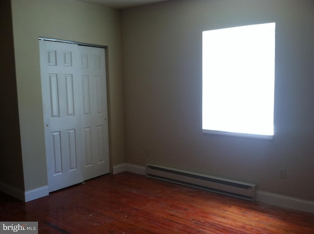 unfurnished bedroom featuring a baseboard radiator, dark hardwood / wood-style floors, and a closet