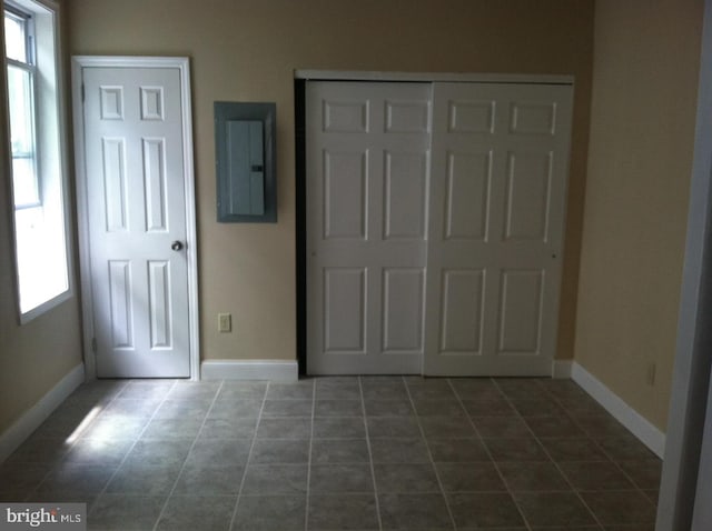 unfurnished bedroom featuring multiple windows, dark tile patterned flooring, electric panel, and a closet