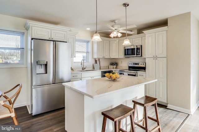 kitchen featuring a kitchen island, appliances with stainless steel finishes, sink, hanging light fixtures, and light stone counters