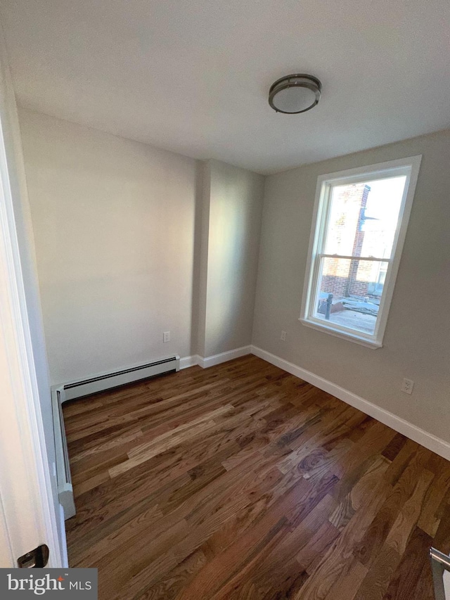 spare room with a baseboard heating unit and dark wood-type flooring