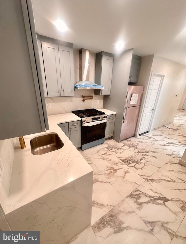 kitchen with sink, gray cabinetry, appliances with stainless steel finishes, light stone countertops, and wall chimney range hood