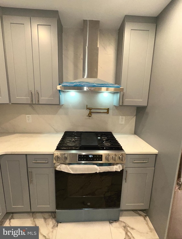 kitchen featuring light stone countertops, gray cabinets, stainless steel gas range oven, and wall chimney range hood