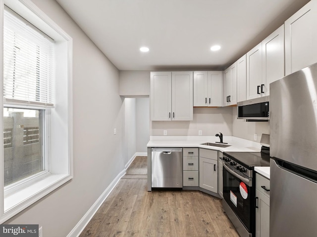 kitchen with appliances with stainless steel finishes, sink, and light wood-type flooring