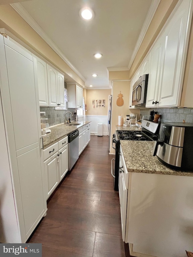 kitchen with appliances with stainless steel finishes, sink, white cabinets, ornamental molding, and light stone countertops