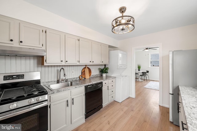 kitchen with stacked washing maching and dryer, ceiling fan with notable chandelier, white cabinetry, sink, and stainless steel appliances