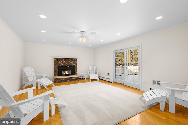 living room with a brick fireplace, a baseboard radiator, ornamental molding, ceiling fan, and hardwood / wood-style floors