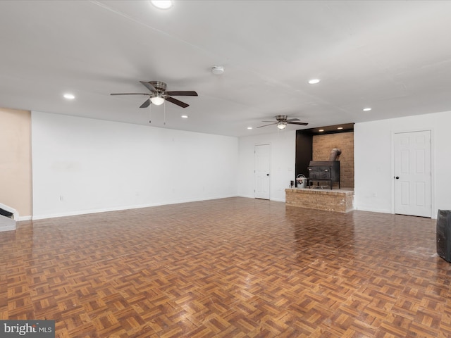 unfurnished living room featuring dark parquet flooring, a wood stove, and ceiling fan