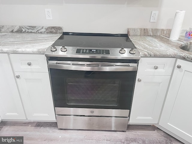 interior details featuring white cabinets, light hardwood / wood-style flooring, and electric range