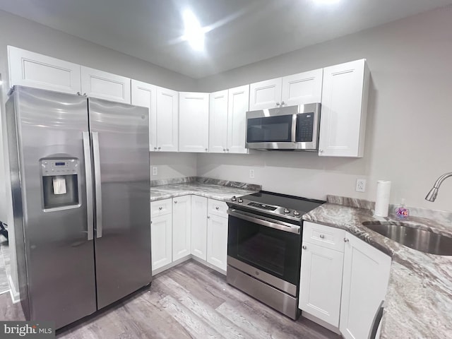 kitchen with appliances with stainless steel finishes, sink, white cabinets, light stone counters, and light hardwood / wood-style flooring