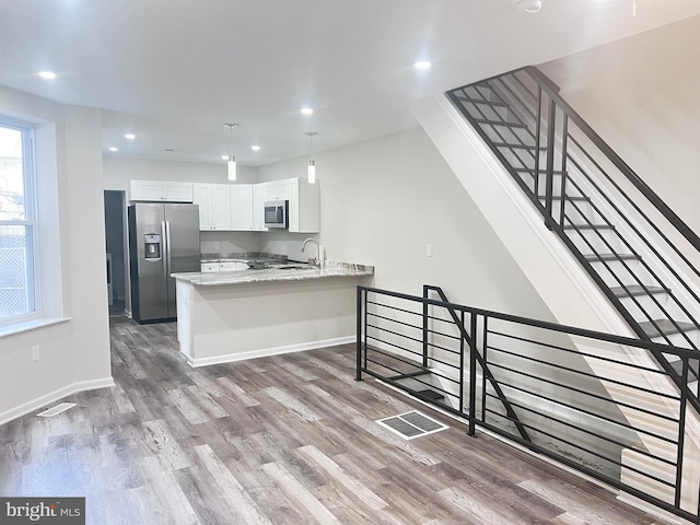 kitchen with stainless steel appliances, light stone countertops, white cabinets, dark hardwood / wood-style flooring, and kitchen peninsula