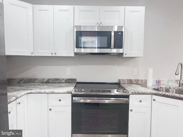 kitchen with white cabinetry, appliances with stainless steel finishes, sink, and stone countertops