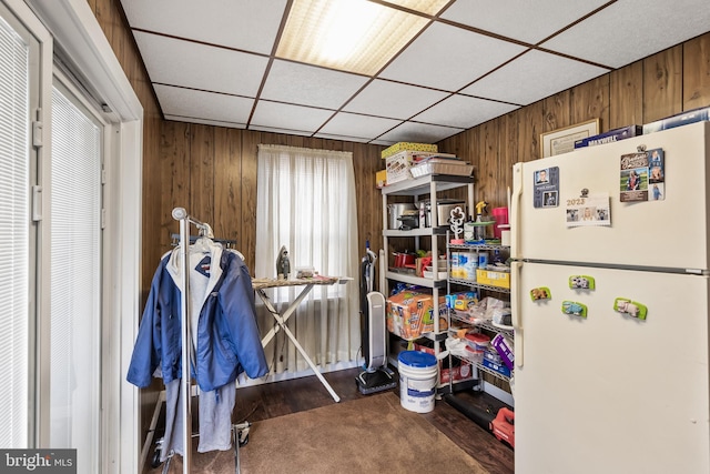 interior space featuring white refrigerator, a paneled ceiling, dark carpet, and wood walls