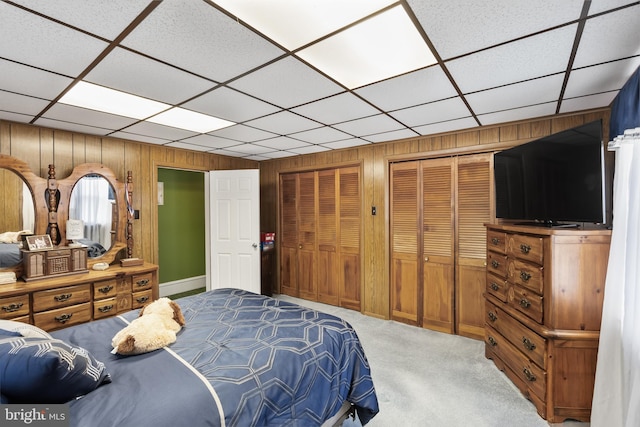 carpeted bedroom with two closets, a drop ceiling, and wooden walls