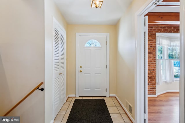 entryway with light tile patterned flooring, brick wall, and a healthy amount of sunlight