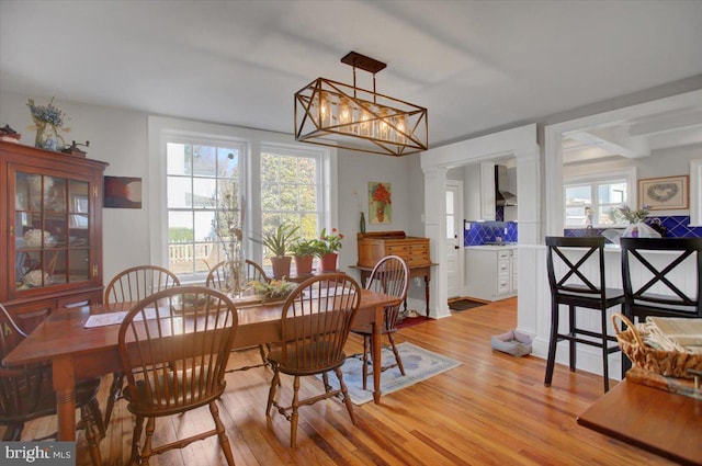 dining room with an inviting chandelier, light hardwood / wood-style flooring, and ornate columns