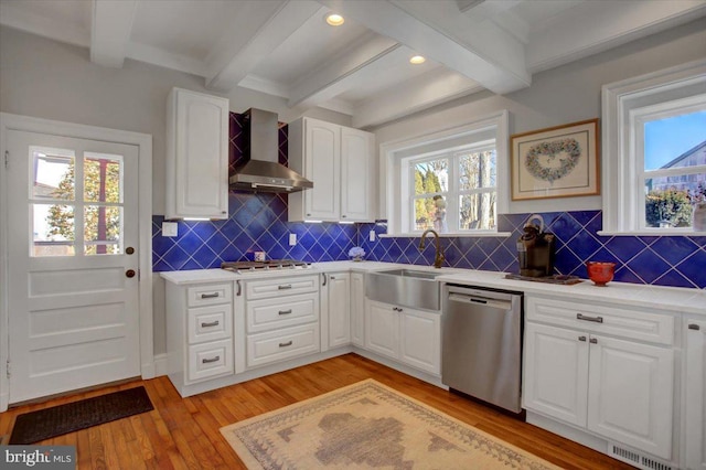 kitchen with sink, white cabinetry, stainless steel appliances, wall chimney exhaust hood, and beamed ceiling