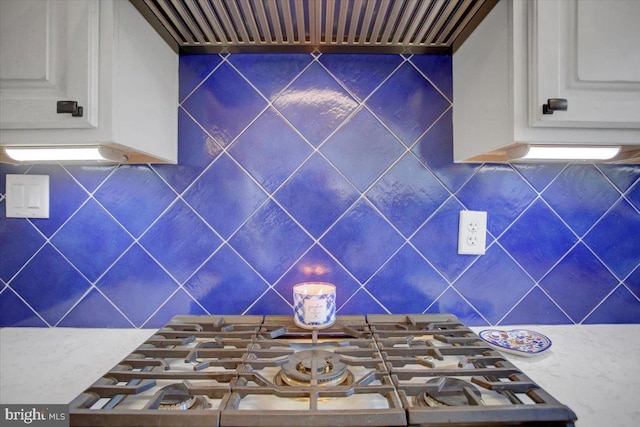 kitchen with white cabinetry, wall chimney exhaust hood, stovetop, and tasteful backsplash