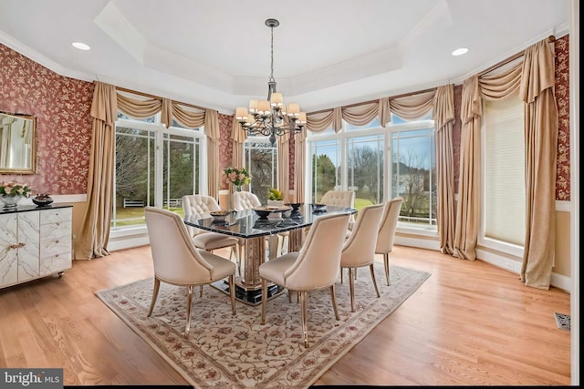 dining area featuring a raised ceiling, ornamental molding, a chandelier, and light hardwood / wood-style flooring