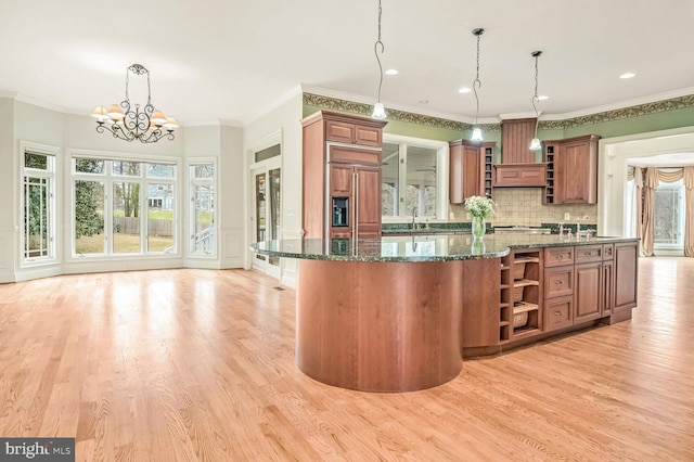 kitchen with pendant lighting, dark stone counters, paneled refrigerator, an inviting chandelier, and light hardwood / wood-style flooring