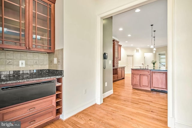 kitchen featuring sink, decorative backsplash, hanging light fixtures, ornamental molding, and light wood-type flooring