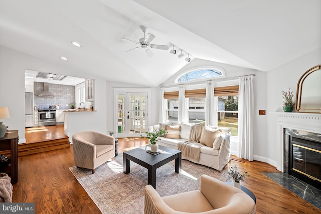 living room with a ceiling fan, vaulted ceiling, wood finished floors, and a high end fireplace